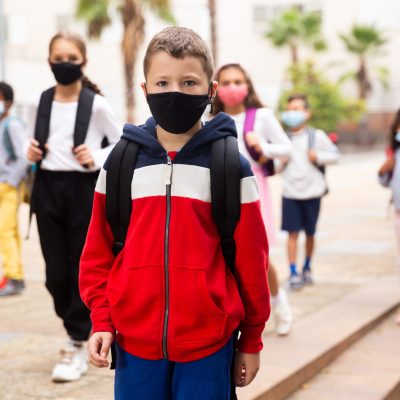 Confident tweenager in protective mask walking with other schoolchildren to school campus after lessons on spring day. Concept of necessary precautions in COVID pandemic